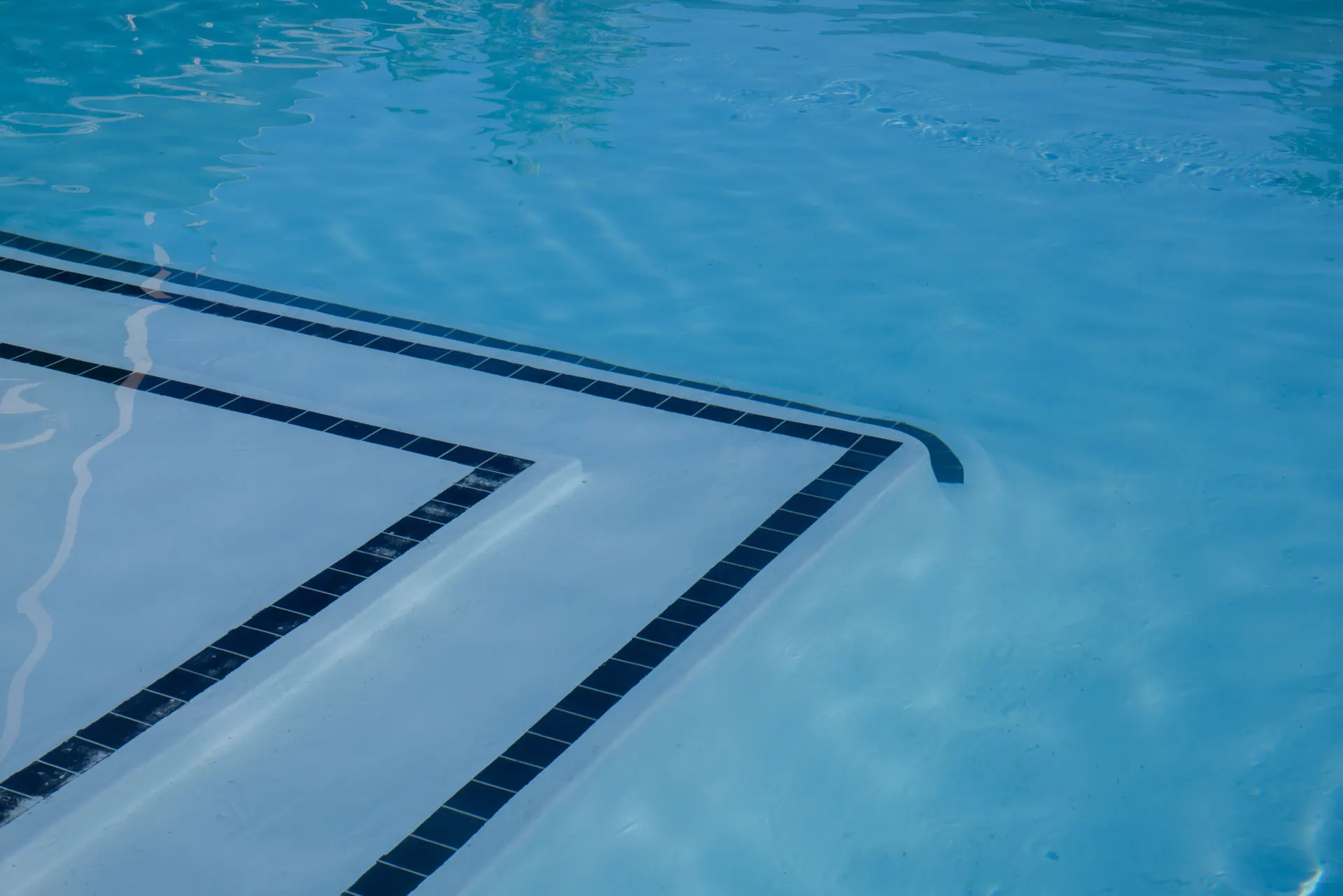 Pool steps edged with dark tiles under clear water
