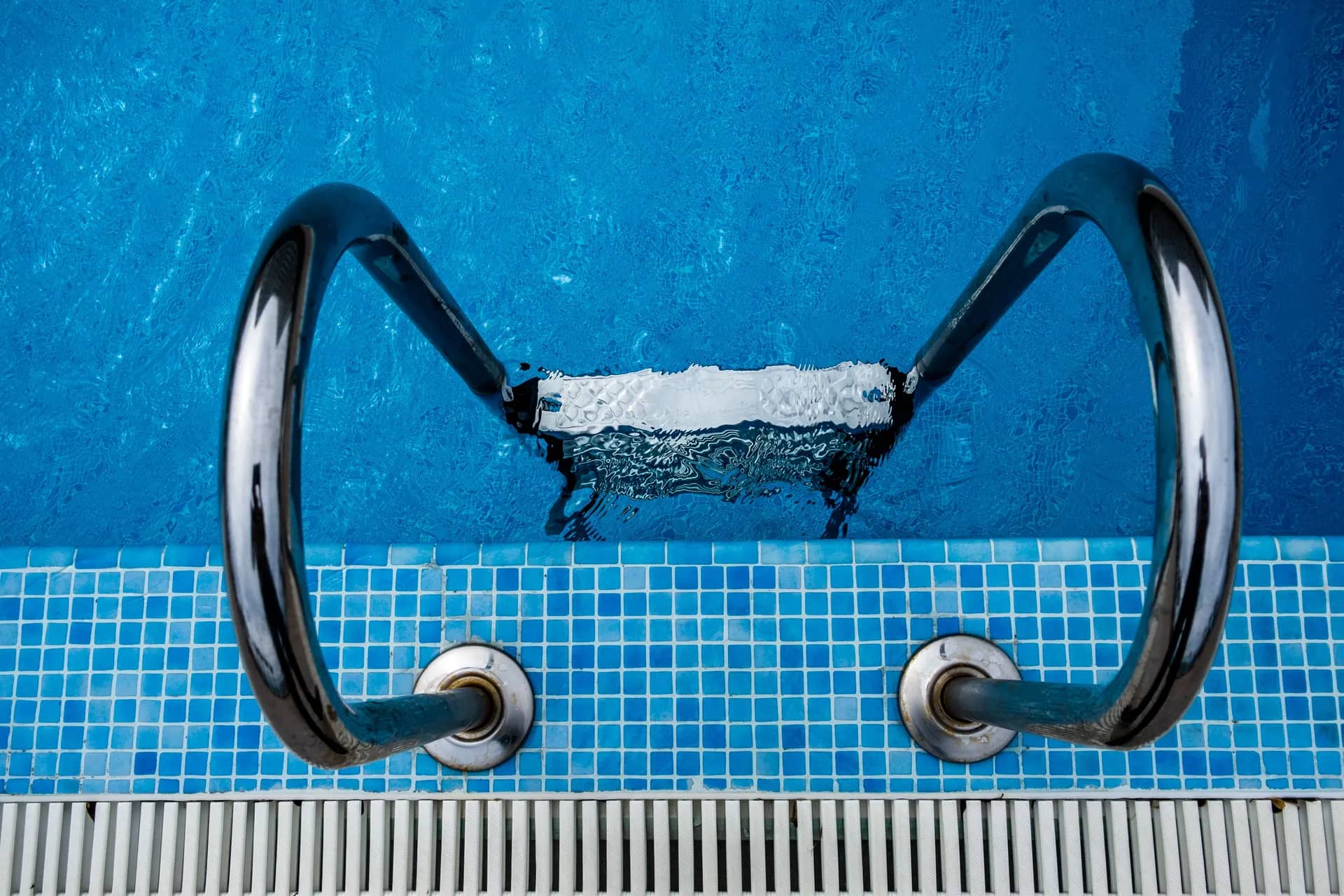 Stainless-steel pool ladder fixed to a mosaic-tiled pool wall